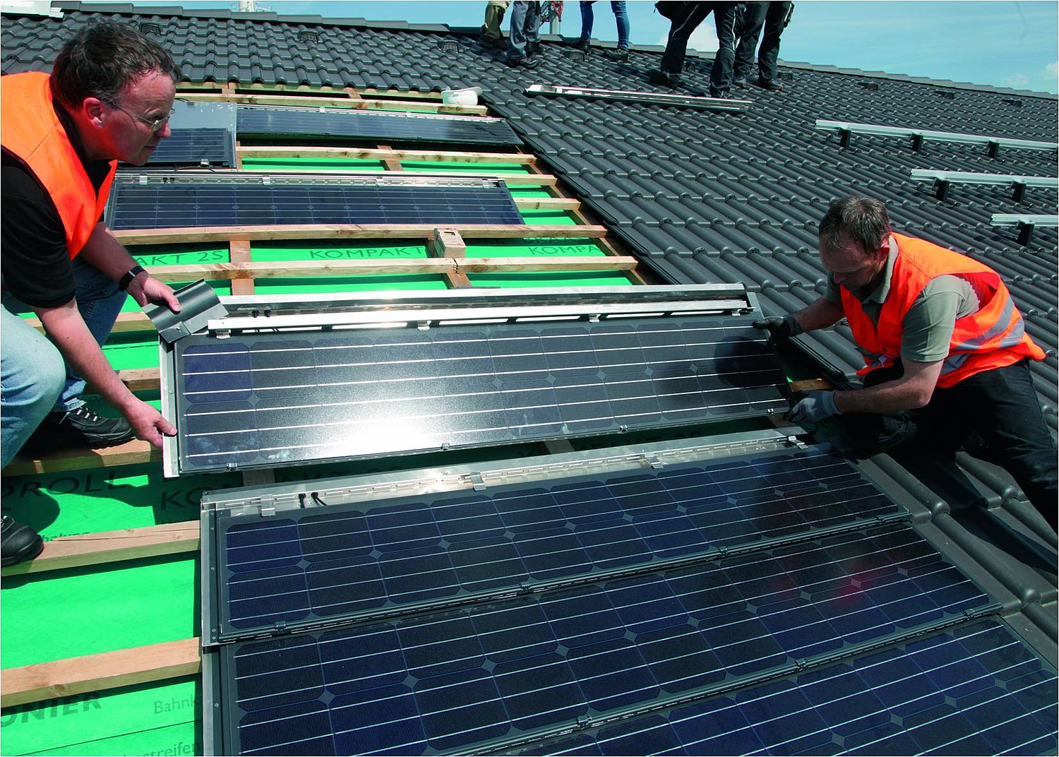 Zwei Arbeiter setzen eine Indach-Phovotolaitk-Platte mit Solarzellen bei der Dacheindeckung ein